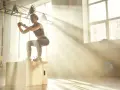 Donna esegue un box jump, dimostrando diversi tipi di forza in palestra, con raggi di sole che filtrano.
