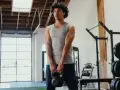 Giovane uomo in palestra, con kettlebell in mano, mostra i suoi muscoli lombari e braccia scolpite.