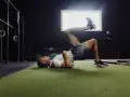 Uomo esegue ponte per gamba singola, un esercizio utile per la fisioterapia per ernia del disco, in palestra.