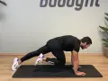 Uomo in posizione di plank, porta un ginocchio al petto, simulando un esercizio di montagna scalatore per un allenamento completo.