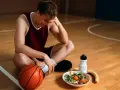Giovane giocatore di basket seduto sul campo, esausto, con pallone, insalata e banana. Potrebbe soffrire di **overtraining sintomi**.