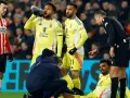 Giocatori di calcio in campo, uno è a terra, assistito dallo staff medico. L'arbitro osserva attentamente, preoccupato per i possibili infortuni nel calcio.