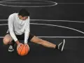 Giovane atleta si allunga sul campo da basket, con una palla arancione. Il suo corpo mostra la necessità di riposo muscolare 48 ore.