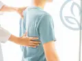 Mani di un medico che esamina la schiena di un paziente, suggerendo uno strappo alla schiena con dolore a respirare.