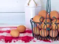 Cesto pieno di uova marroni, pronte per mangiare uova tutti i giorni. Due uova su una tovaglia a quadri rossa.