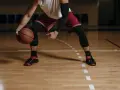 Giocatore di basket in posizione bassa, con palla in mano. Le gambe, impegnate in esercizi di rinforzo muscolare arti inferiori, sono protette da calzettoni neri.
