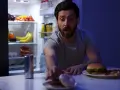 Uomo con espressione sorpresa allunga la mano verso ciambelle e pizza, con il frigorifero aperto alle sue spalle, una tentazione notturna che sfida la finestra metabolica.