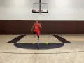 Giovane atleta in divisa arancione esegue uno degli **10 esercizi di riscaldamento** su un campo da basket, con coni gialli a terra.