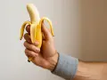 Una mano con polsino grigio tiene una banana sbucciata, pronta per la banana prima della partita.