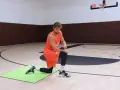 Atleta in ginocchio su un tappetino verde, esegue un esercizio di riscaldamento caviglie in palestra.