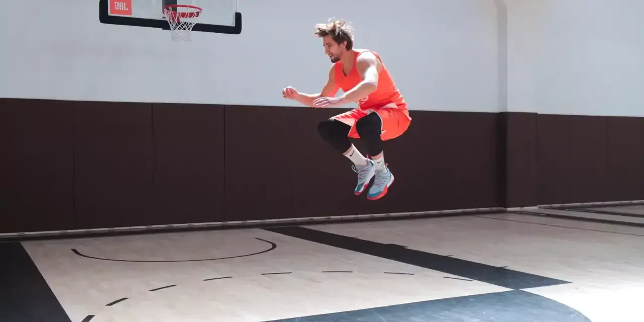Atleta in aria, in pieno allenamento contro resistenza, su un campo da basket.