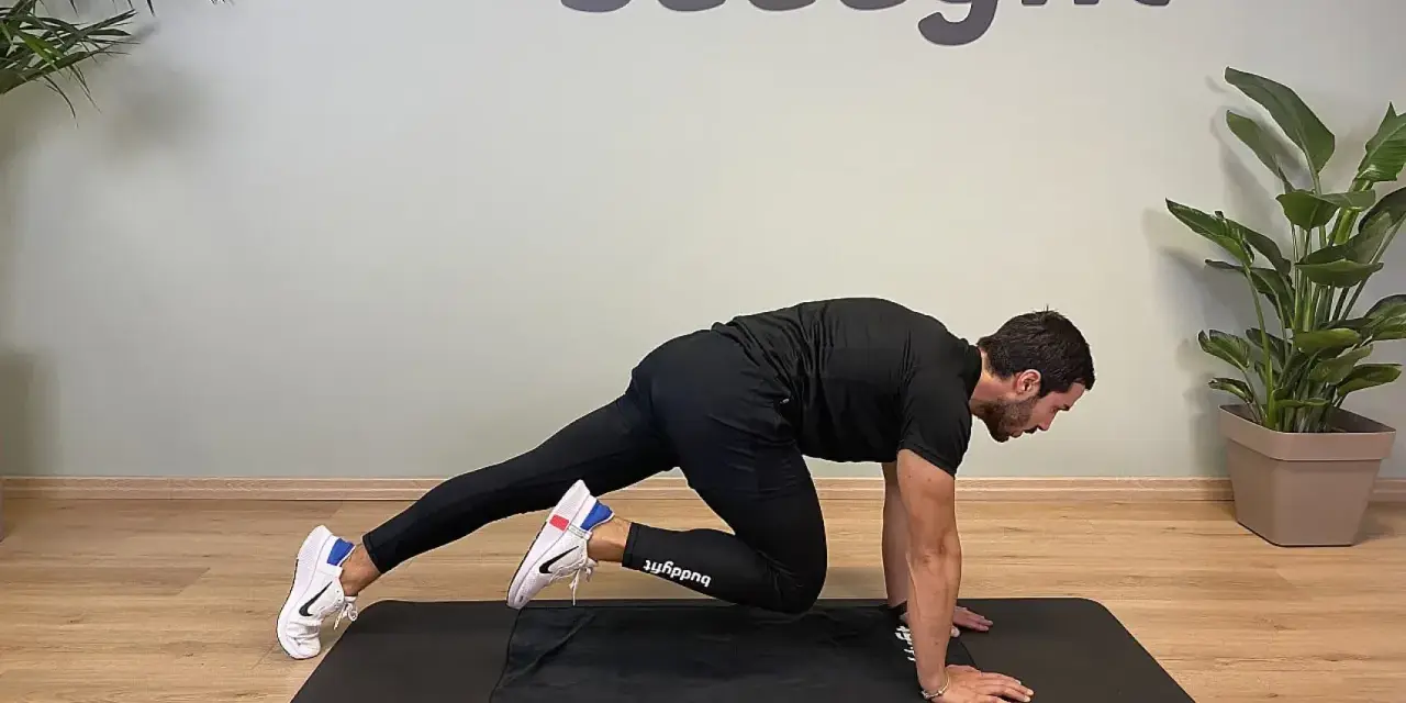 Uomo in posizione di plank, porta un ginocchio al petto, simulando un esercizio di montagna scalatore per un allenamento completo.