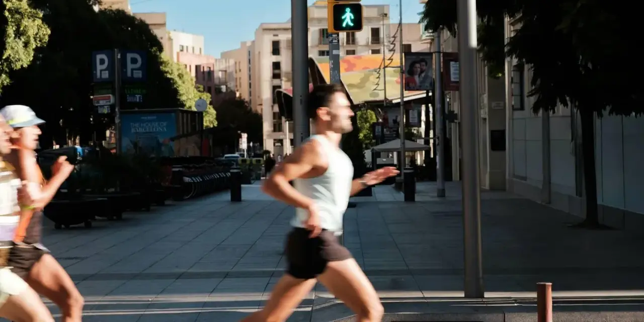 Corridori in città, un uomo corre con un semaforo pedonale verde. Il **talk test** è superato, respira bene.