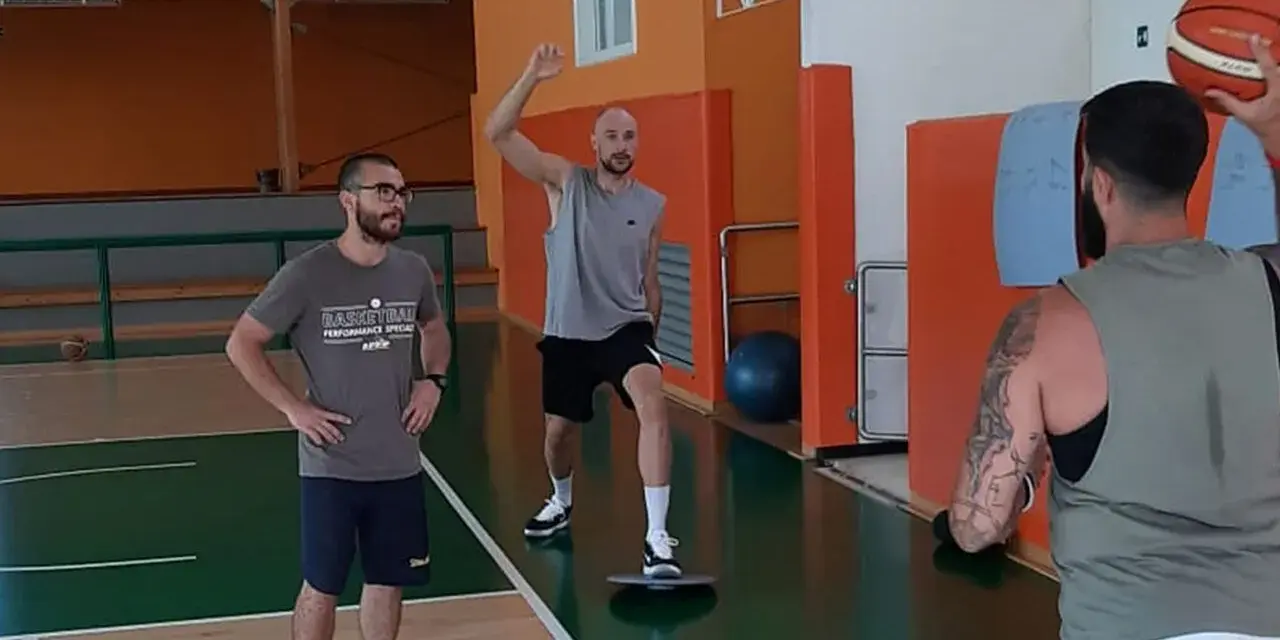 Allenamento in palestra: un uomo esegue torsioni del busto su una tavoletta di equilibrio, mentre un altro lo osserva.