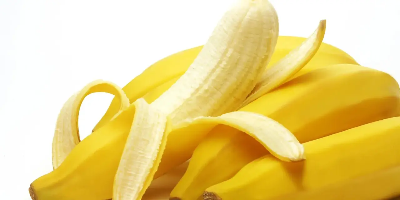Un grappolo di banane gialle, una parzialmente sbucciata, che fa pensare a quanto potassio contiene una banana.