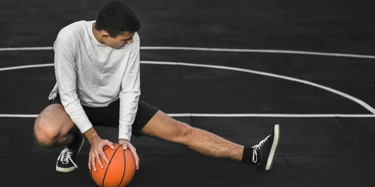 Giovane atleta si allunga sul campo da basket, con una palla arancione. Il suo corpo mostra la necessità di riposo muscolare 48 ore.