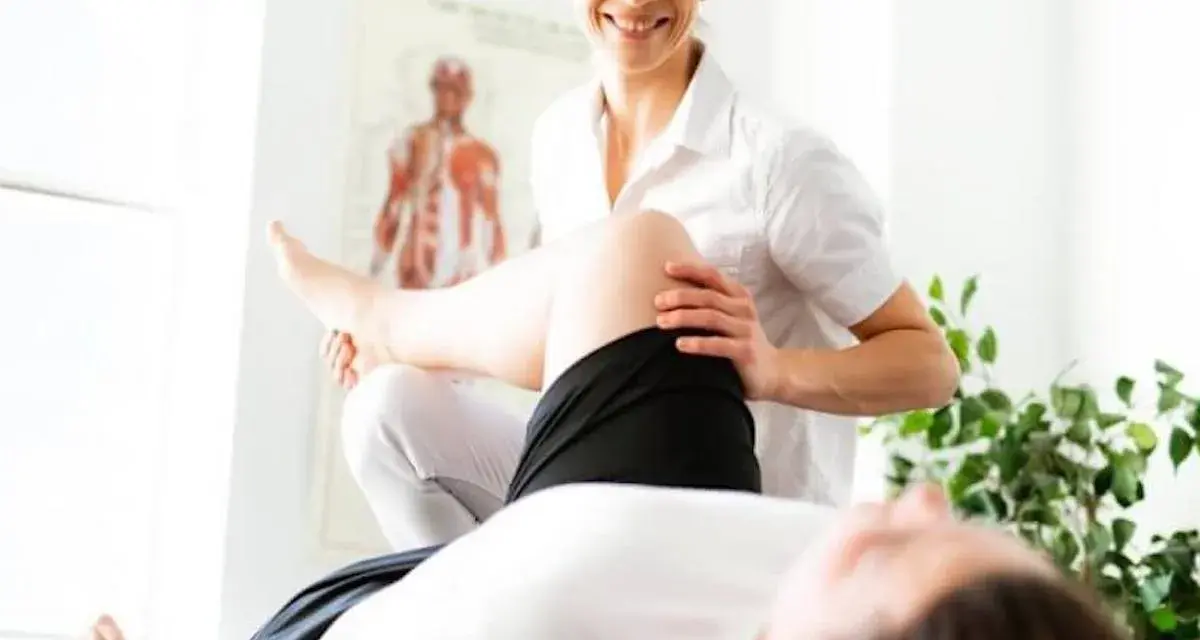 Un fisioterapista esegue un trattamento alla gamba di un paziente, con un poster anatomico sullo sfondo.
