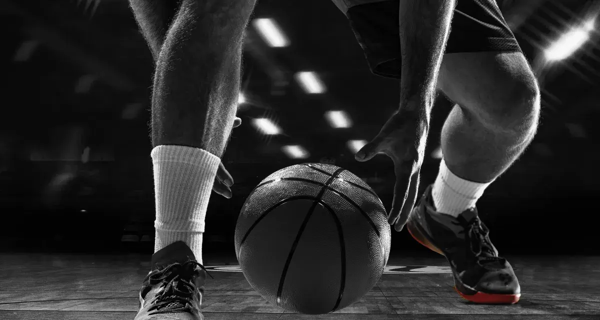 Giocatore di basket in azione, concentrato sul palleggio. Allenarsi per migliorare il fiato è fondamentale per vincere.
