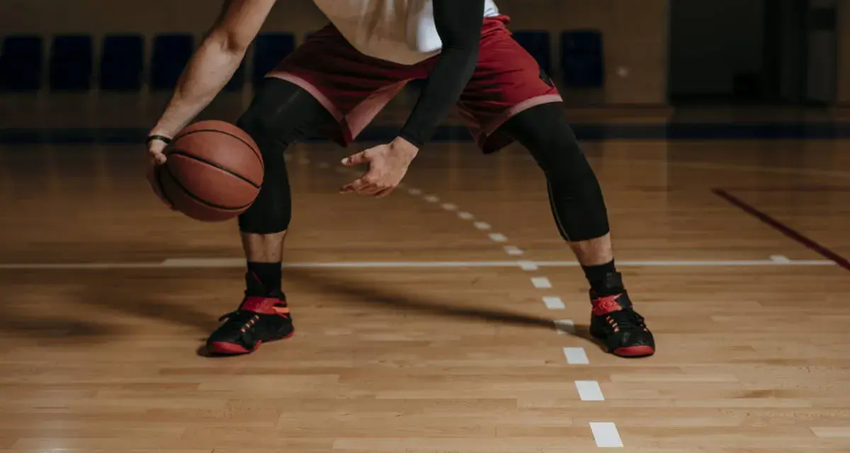 Giocatore di basket in posizione bassa, con palla in mano. Le gambe, impegnate in esercizi di rinforzo muscolare arti inferiori, sono protette da calzettoni neri.