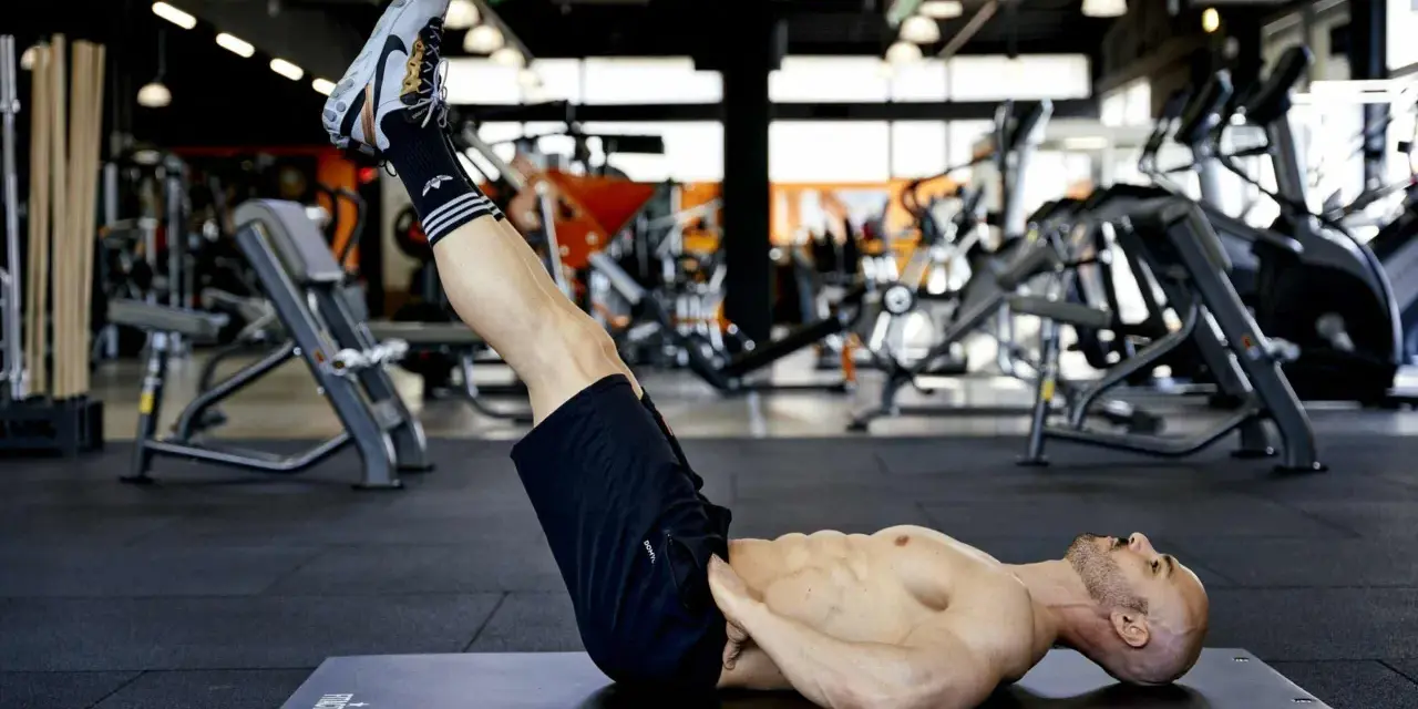 Uomo muscoloso esegue reverse crunch su panca in palestra, concentrato sull'allenamento addominale.