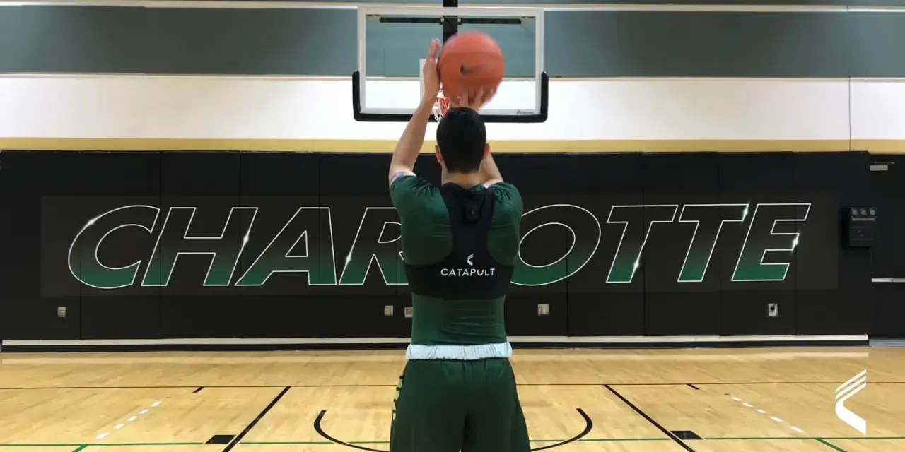Basketball player in green uniform shooting a basketball in a gym with "CHARLOTTE" logo on the wall.