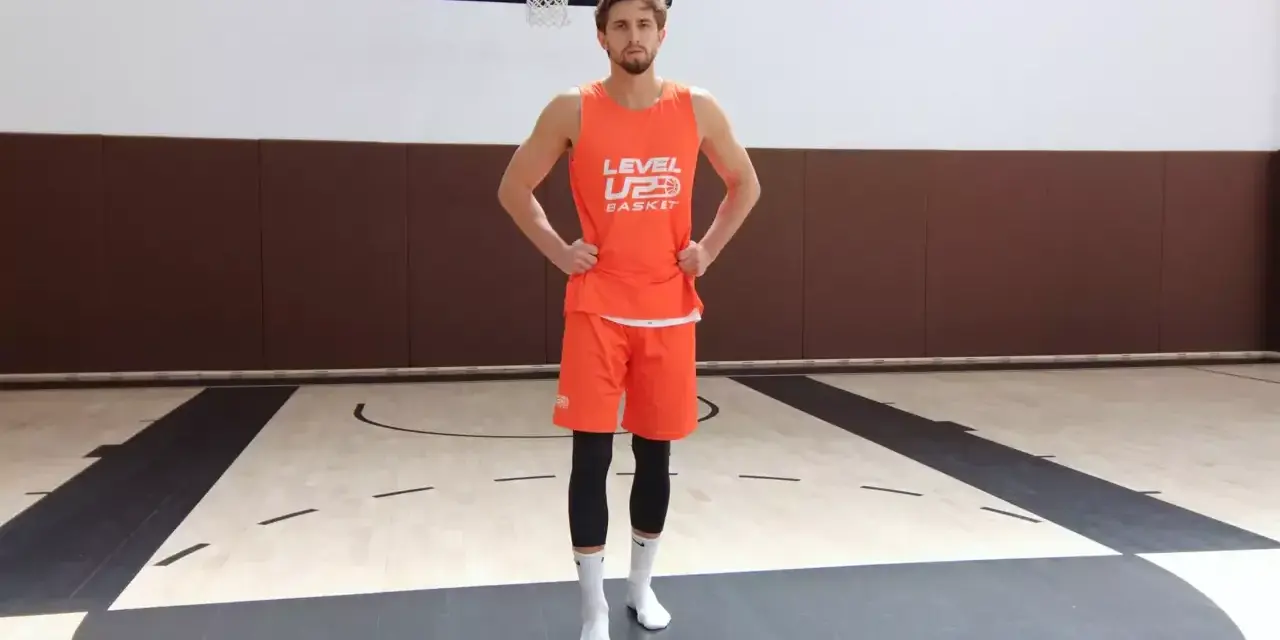 Giovane giocatore di basket in tenuta arancione, pronto per esercizi per i piedi sul campo.