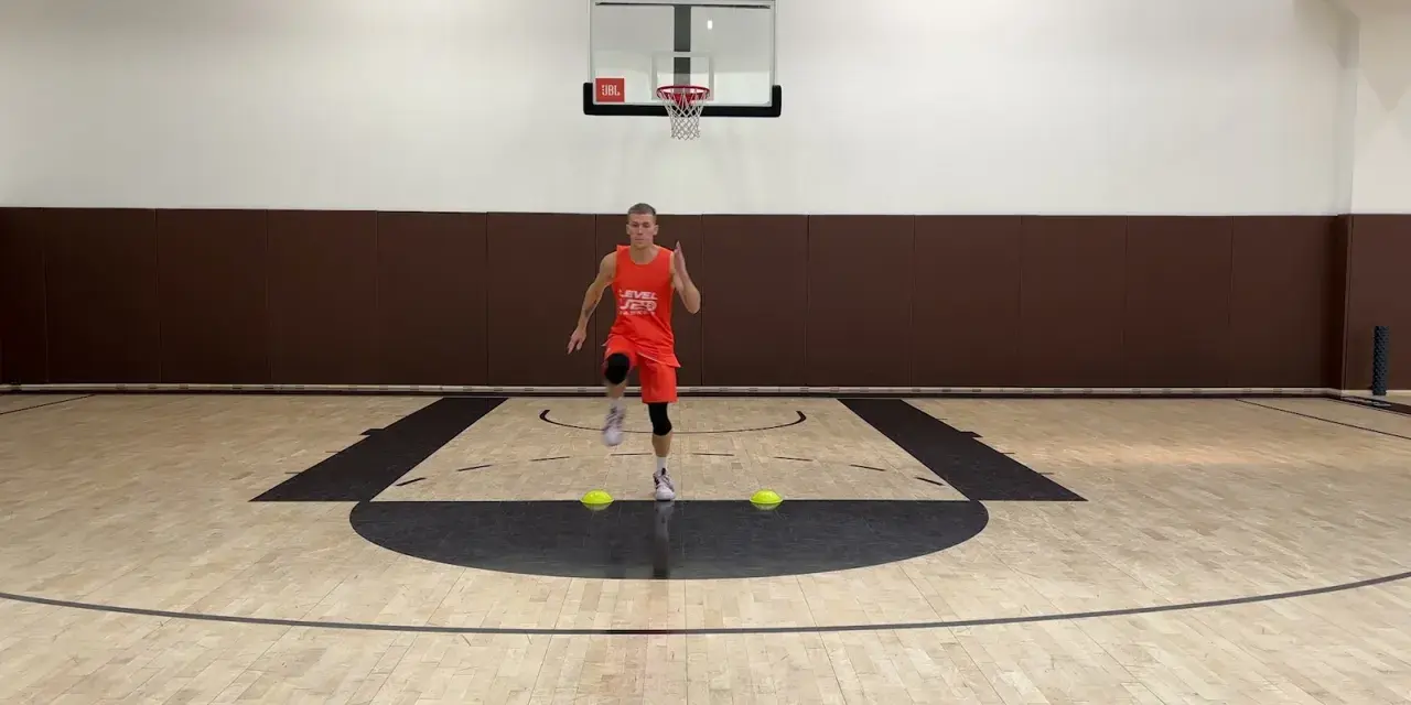 Giovane atleta in divisa arancione esegue uno degli **10 esercizi di riscaldamento** su un campo da basket, con coni gialli a terra.