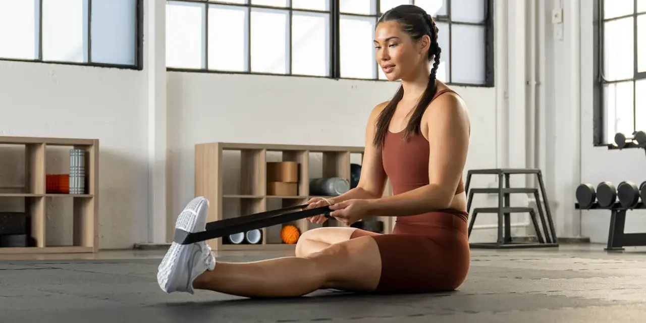 Donna esegue allungamento polpacci con elastico in palestra.