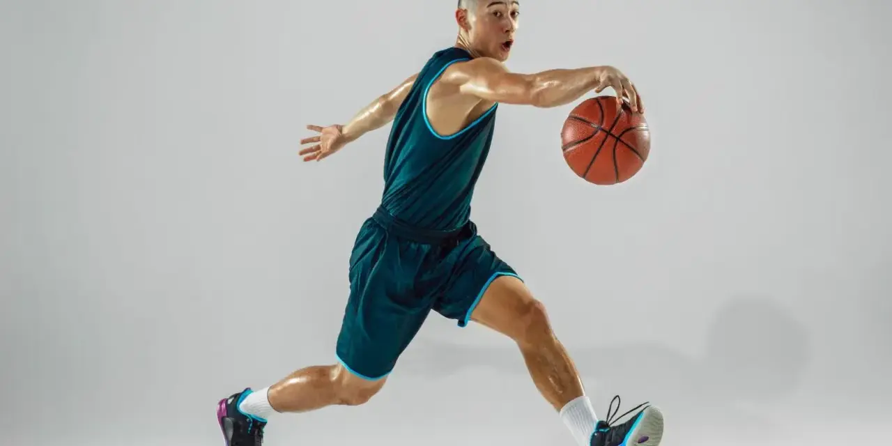 Giovane giocatore di basket in azione, con la palla in mano. La sua postura dinamica è il risultato di allenamenti e test posturali mirati.