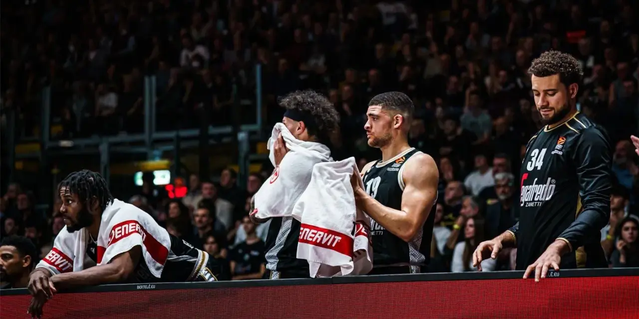 Giocatori di basket in panchina, asciugandosi il sudore con asciugamani. Un promemoria che anche gli atleti hanno bisogno di recupero e proteine in un giorno intenso.