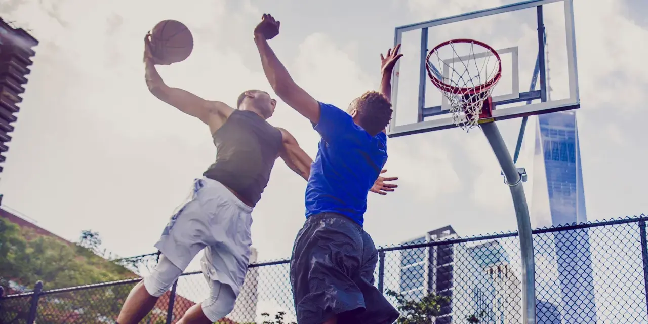 Due giocatori di basket saltano per un canestro. L'energia che li spinge, come i carboidrati complessi quali sono, è visibile in ogni movimento.