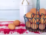 Cesto pieno di uova marroni, pronte per mangiare uova tutti i giorni. Due uova su una tovaglia a quadri rossa.