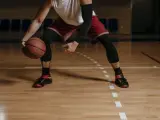 Giocatore di basket in posizione bassa, con palla in mano. Le gambe, impegnate in esercizi di rinforzo muscolare arti inferiori, sono protette da calzettoni neri.
