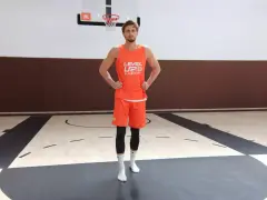 Giocatore di basket in tenuta arancione, mani sui fianchi, con enfasi sui muscoli del bacino laterali.