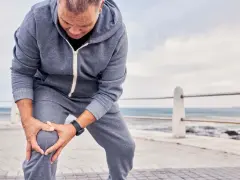 Uomo con tuta grigia si tiene il ginocchio, preoccupato per come sbloccare un ginocchio bloccato.