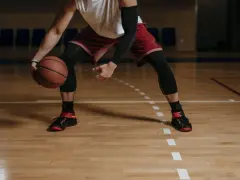 Giocatore di basket in posizione bassa, con palla in mano. Le gambe, impegnate in esercizi di rinforzo muscolare arti inferiori, sono protette da calzettoni neri.