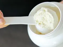 Mano che preleva proteine in polvere da un barattolo bianco con un misurino. Ideale per il recupero post-allenamento.