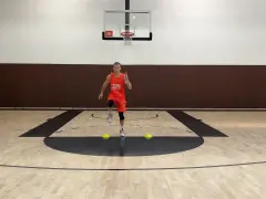 Giovane atleta in divisa arancione esegue uno degli **10 esercizi di riscaldamento** su un campo da basket, con coni gialli a terra.
