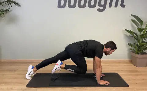 Uomo in posizione di plank, porta un ginocchio al petto, simulando un esercizio di montagna scalatore per un allenamento completo.