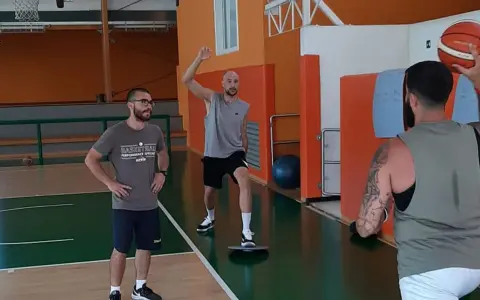 Allenamento in palestra: un uomo esegue torsioni del busto su una tavoletta di equilibrio, mentre un altro lo osserva.
