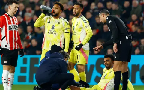 Giocatori di calcio in campo, uno è a terra, assistito dallo staff medico. L'arbitro osserva attentamente, preoccupato per i possibili infortuni nel calcio.