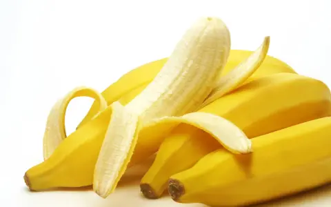 Un grappolo di banane gialle, una parzialmente sbucciata, che fa pensare a quanto potassio contiene una banana.