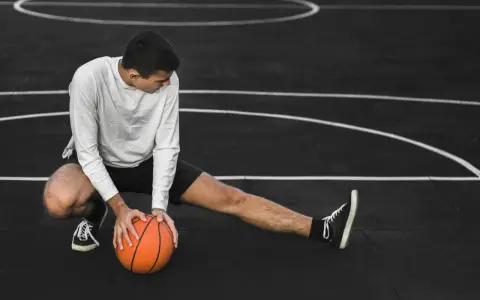 Giovane atleta si allunga sul campo da basket, con una palla arancione. Il suo corpo mostra la necessità di riposo muscolare 48 ore.