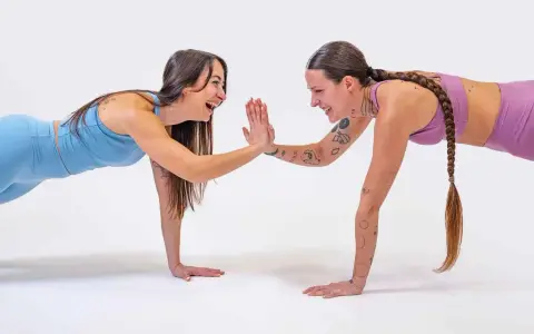 Due donne in posizione di plank si danno il cinque, un allenamento post parto che rafforza il corpo e lo spirito.