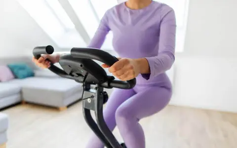 Donna in tuta viola pedala su cyclette, riabilitazione post protesi ginocchio.