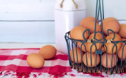 Cesto pieno di uova marroni, pronte per mangiare uova tutti i giorni. Due uova su una tovaglia a quadri rossa.