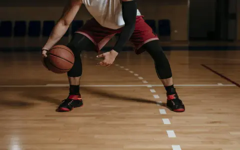 Giocatore di basket in posizione bassa, con palla in mano. Le gambe, impegnate in esercizi di rinforzo muscolare arti inferiori, sono protette da calzettoni neri.