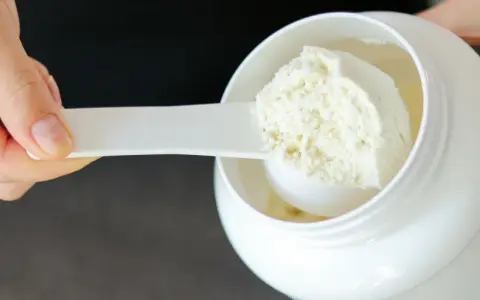Mano che preleva proteine in polvere da un barattolo bianco con un misurino. Ideale per il recupero post-allenamento.
