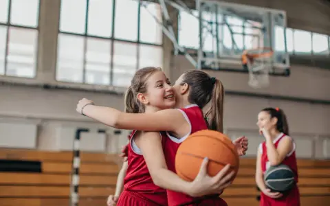 Due giocatrici di basket si abbracciano, una tiene un pallone. Forse si allenano con esercizi mobilità anche e bacino.