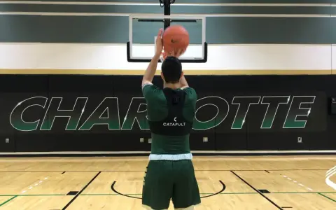 Basketball player in green uniform shooting a basketball in a gym with "CHARLOTTE" logo on the wall.